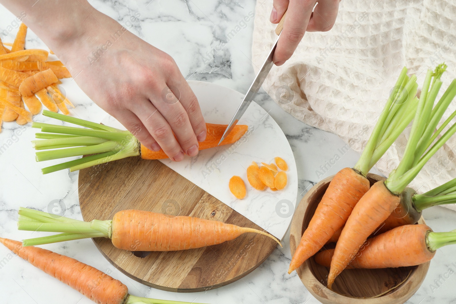 Photo of Woman cutting fresh carrot at white marble table, top view