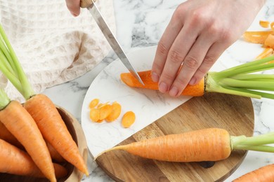 Photo of Woman cutting fresh carrot at white marble table, above view