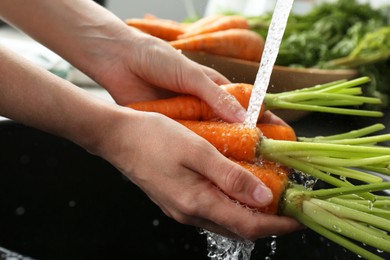 Photo of Woman washing fresh carrots under tap water in above sink indoors, closeup