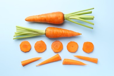 Whole and cut fresh carrots on light background, flat lay