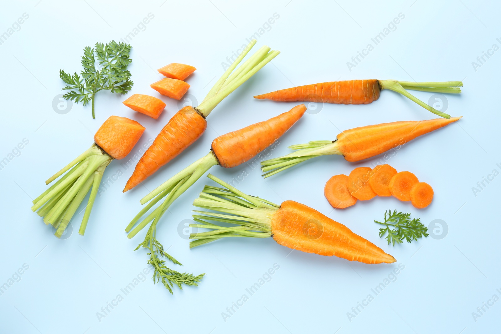 Photo of Whole and cut fresh carrots with green leaves on light background, flat lay