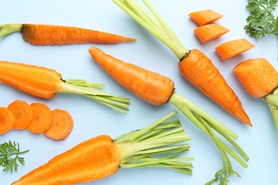 Whole and cut fresh carrots on light background, flat lay