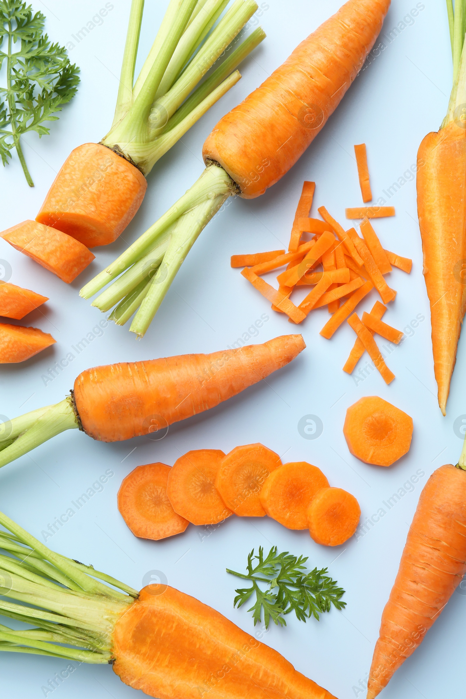 Photo of Whole and cut fresh carrots with green leaves on light background, flat lay