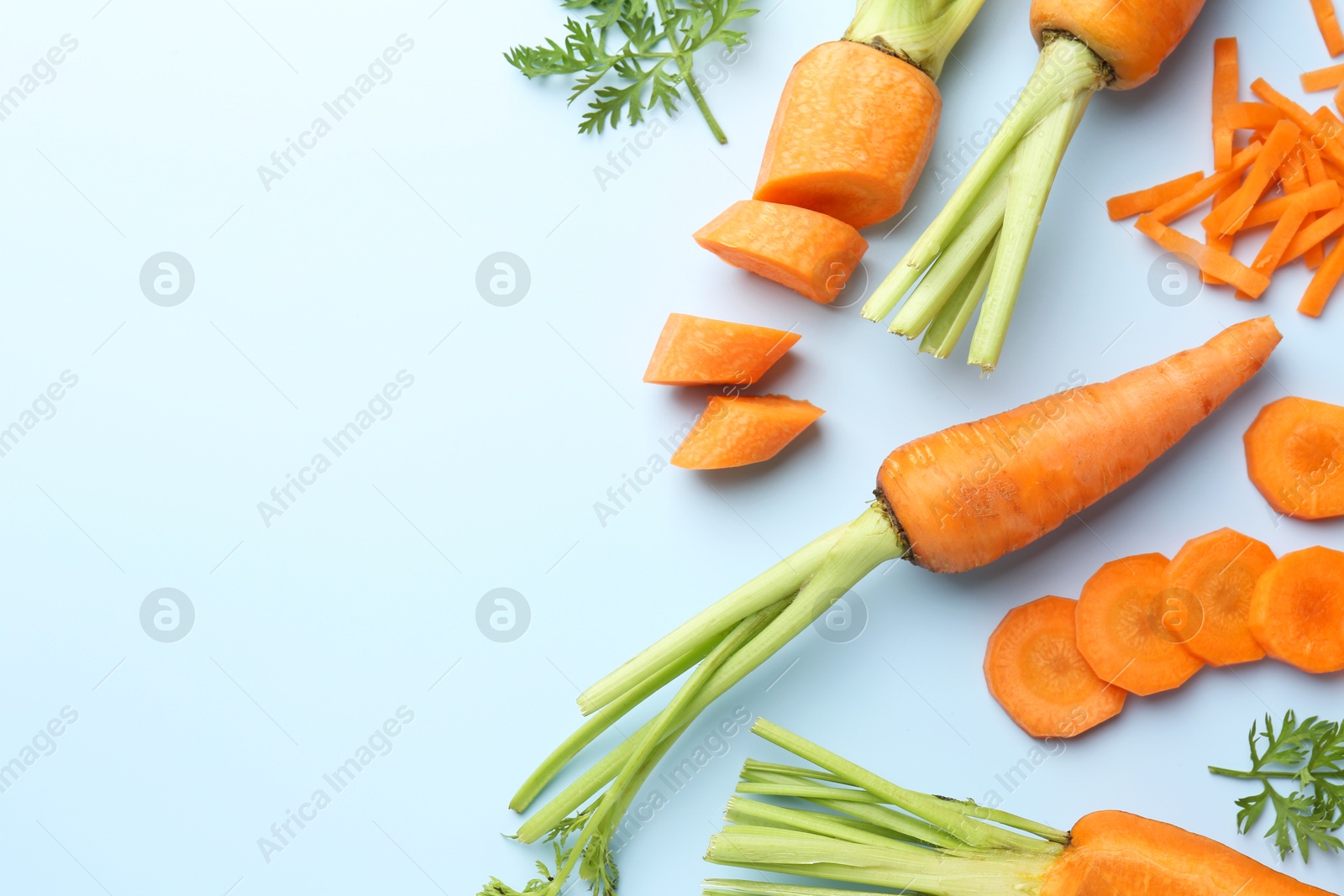 Photo of Whole and cut fresh carrots with green leaves on light background, flat lay. Space for text