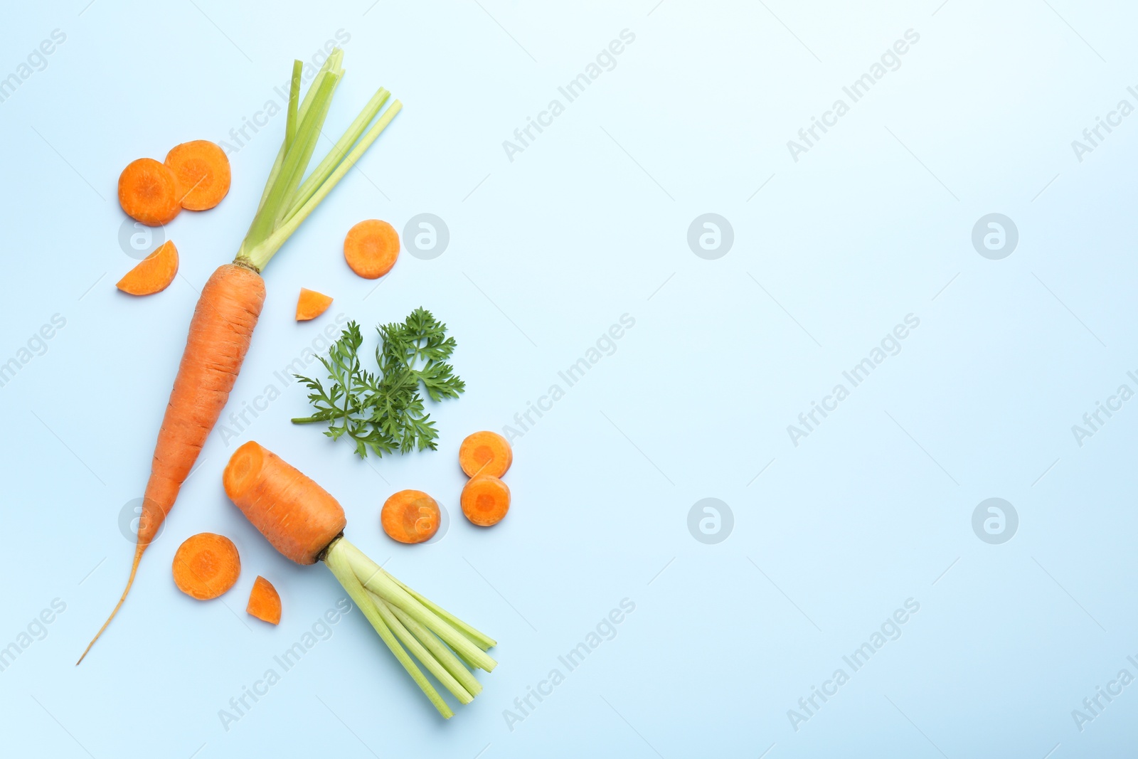 Photo of Whole and cut fresh carrots with green leaf on light background, flat lay. Space for text