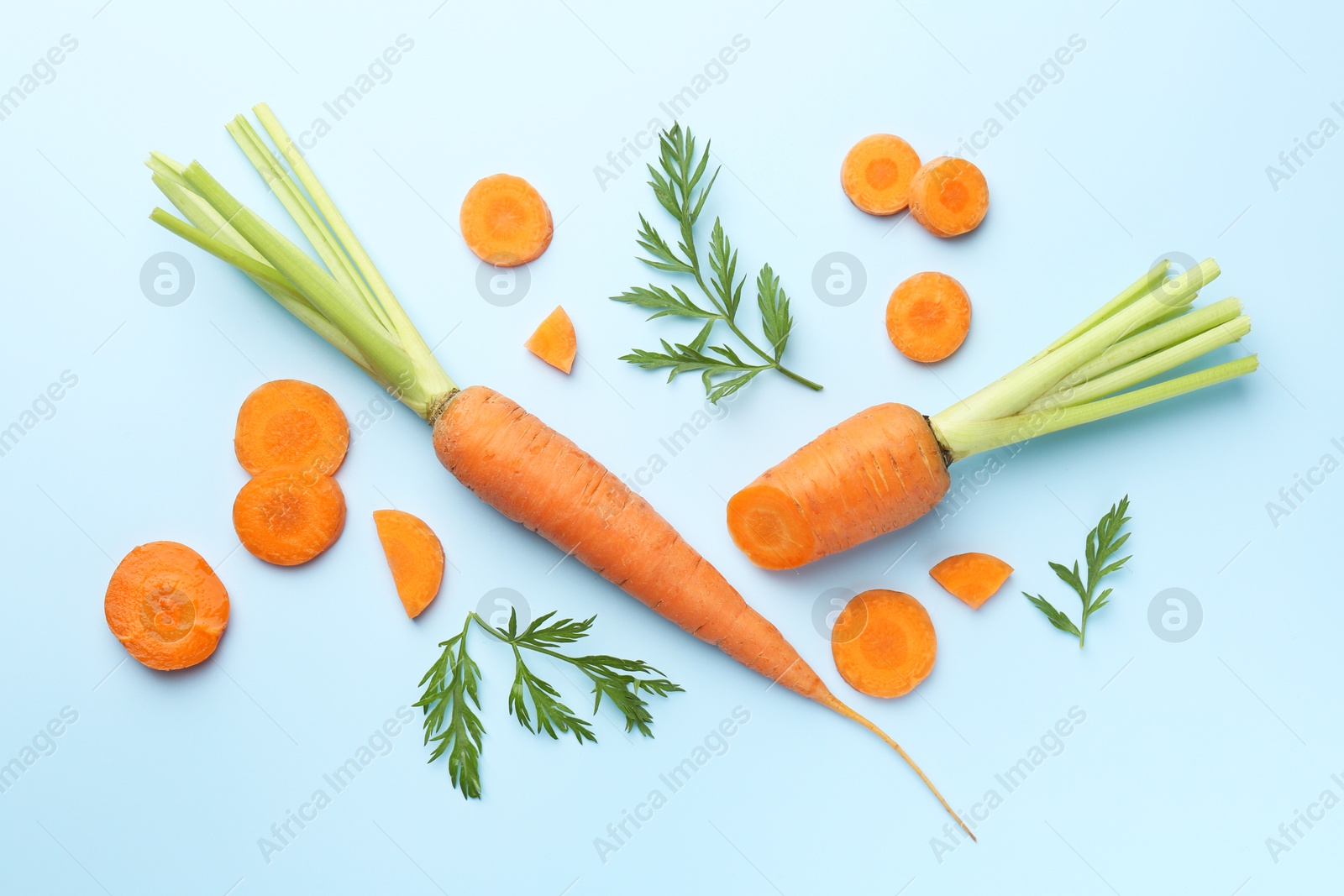 Photo of Whole and cut fresh carrots with green leaves on light background, flat lay