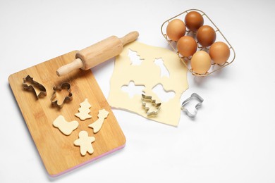 Photo of Raw dough, cookie cutters, board, eggs and rolling pin on white background, above view