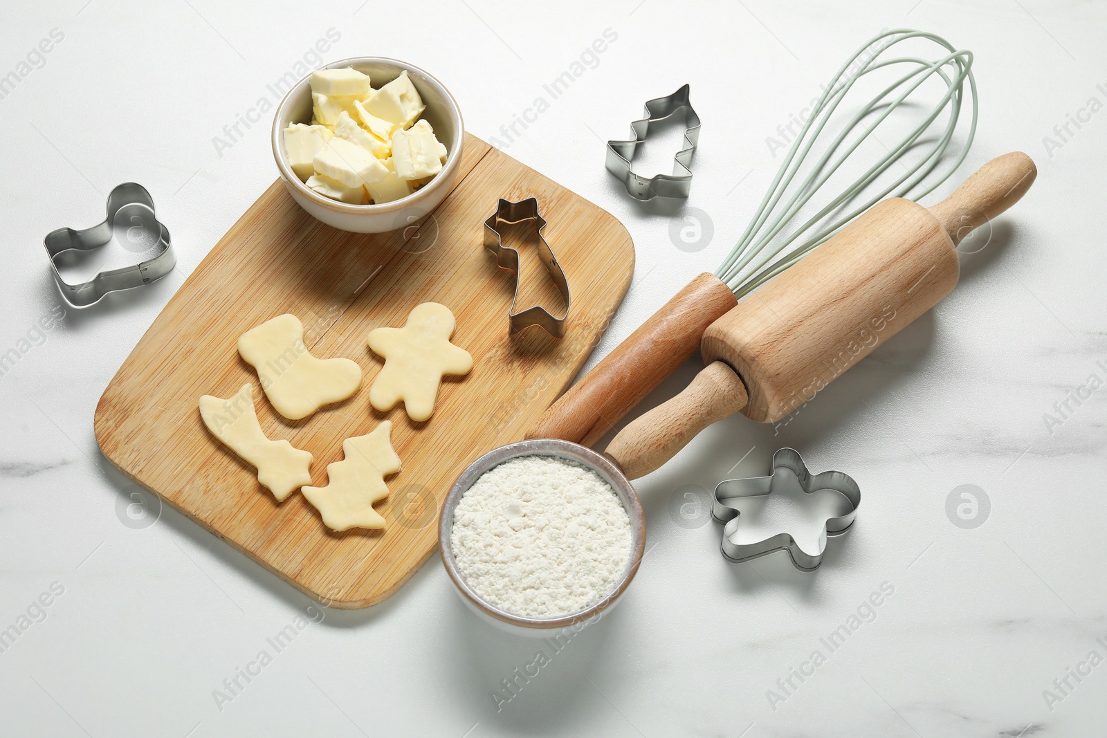 Photo of Raw cookies, cutters, whisk, ingredients and rolling pin on white marble table, above view