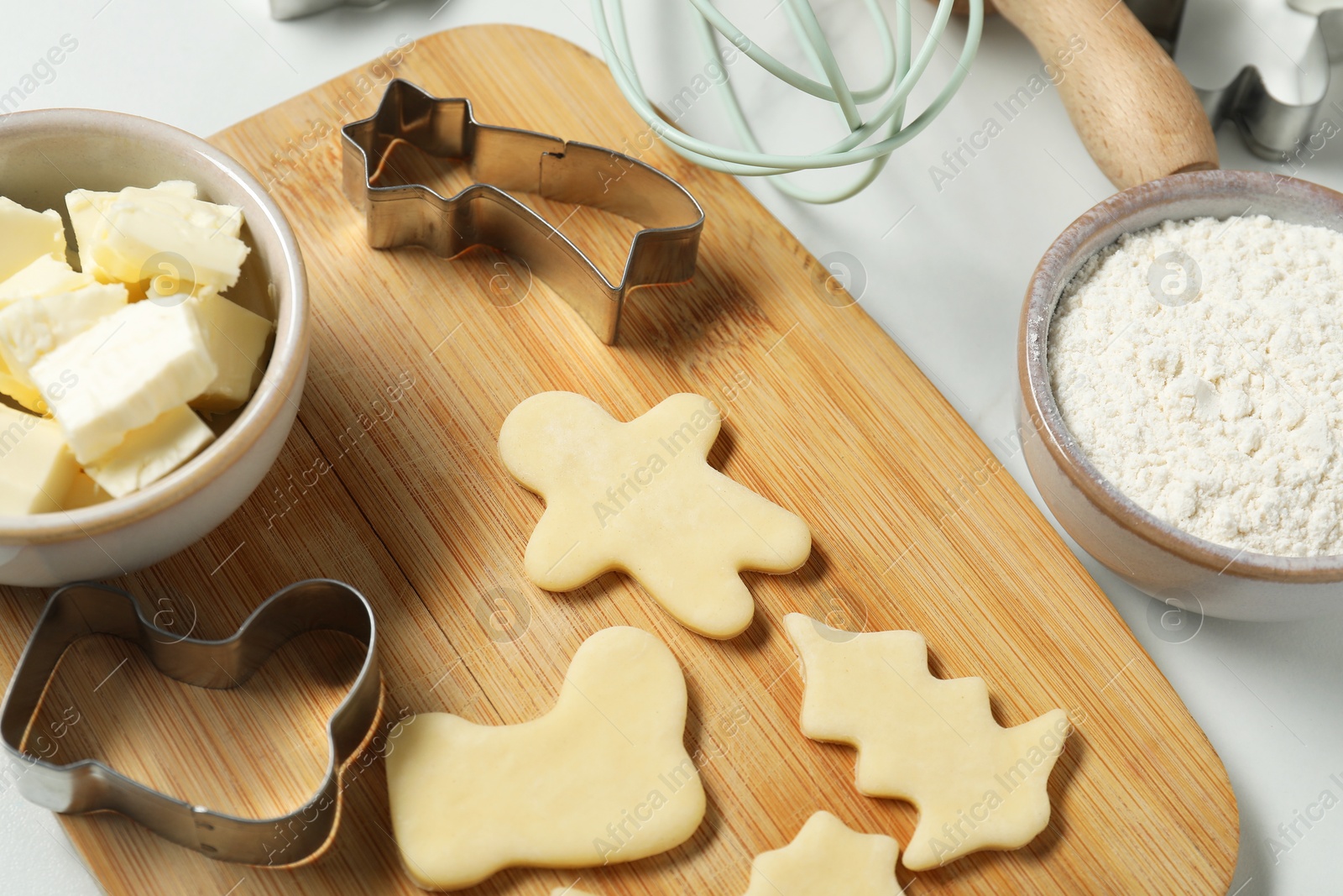 Photo of Raw cookies, cutters, butter and flour on white table, closeup