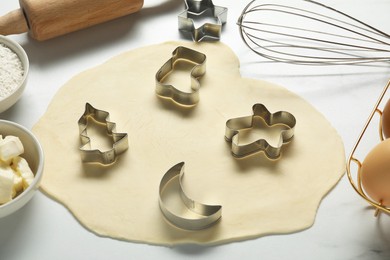 Raw dough and cookie cutters on white table, closeup