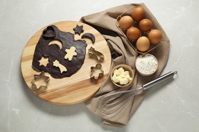 Raw dough, cookie cutters, whisk and ingredients on grey marble table, top view