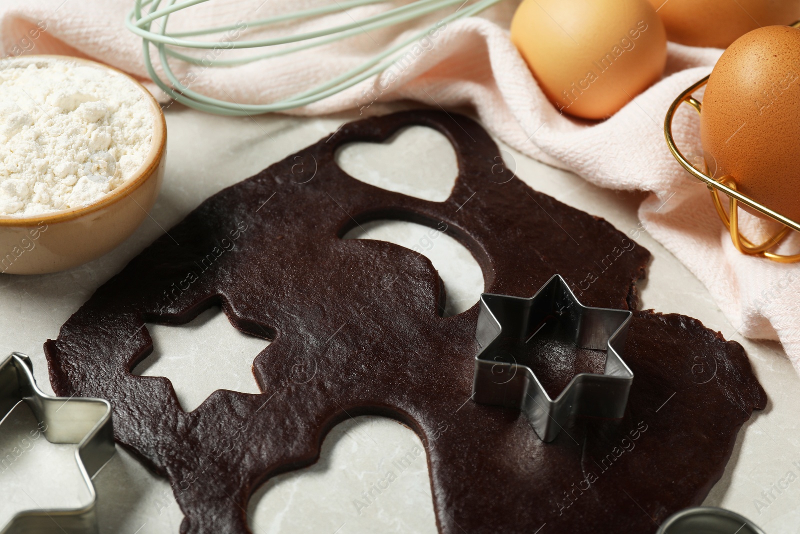 Photo of Raw dough, flour and cookie cutters on light table, closeup