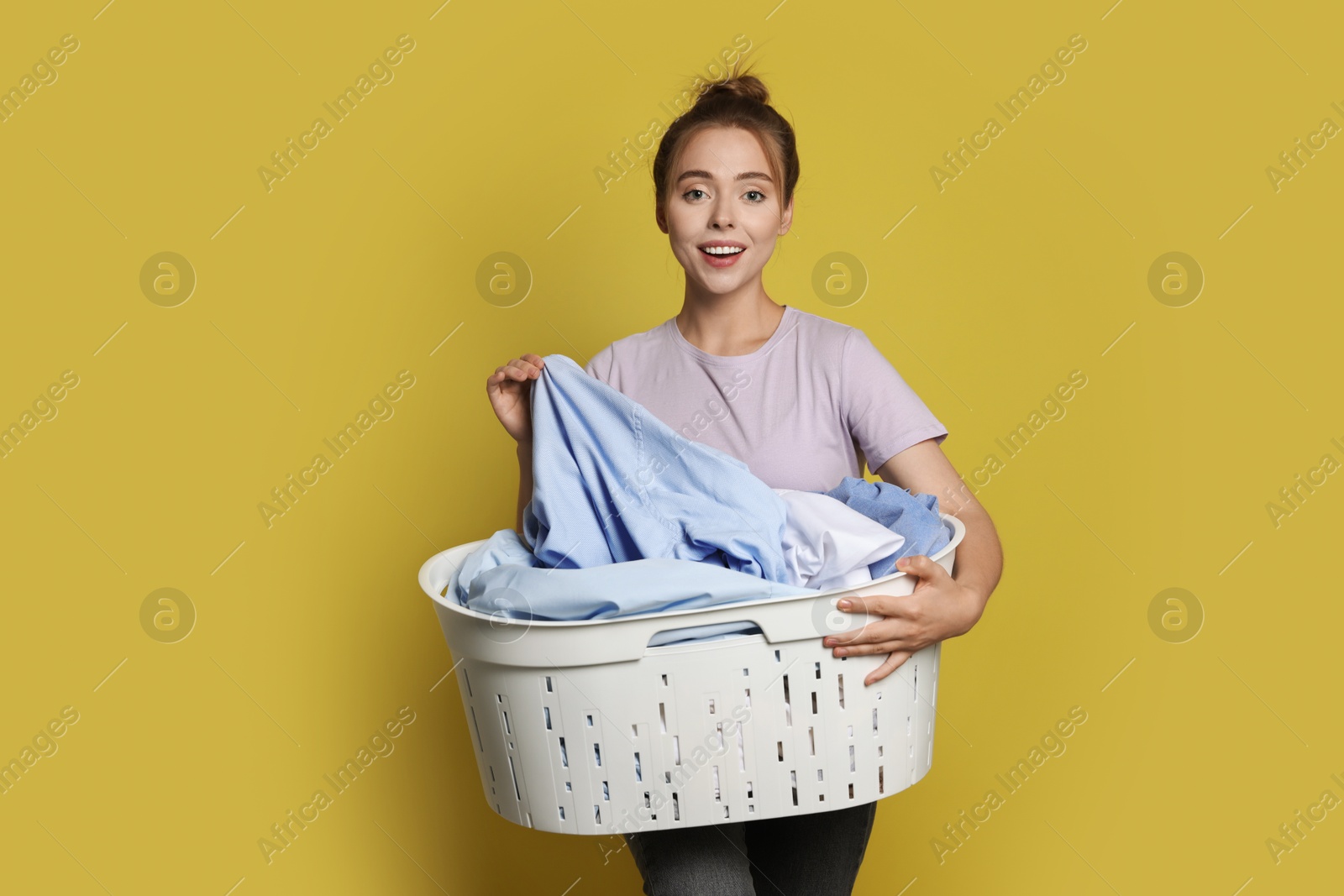 Photo of Happy young housewife with basket full of laundry on yellow background