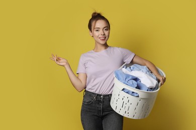 Photo of Happy young housewife with basket full of laundry on yellow background