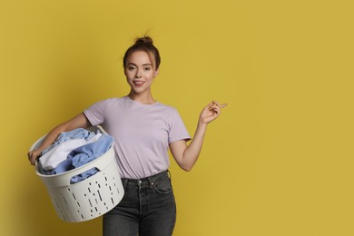 Photo of Happy young housewife with basket full of laundry on yellow background. Space for text