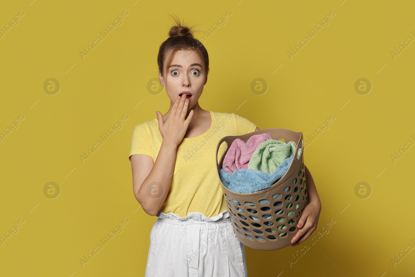 Photo of Emotional housewife with basket full of laundry on yellow background