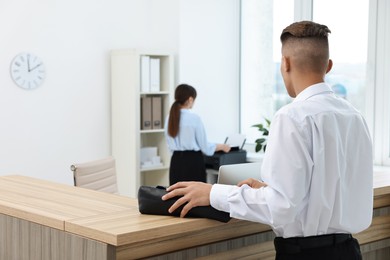 Photo of Professional receptionist and client in office, back view