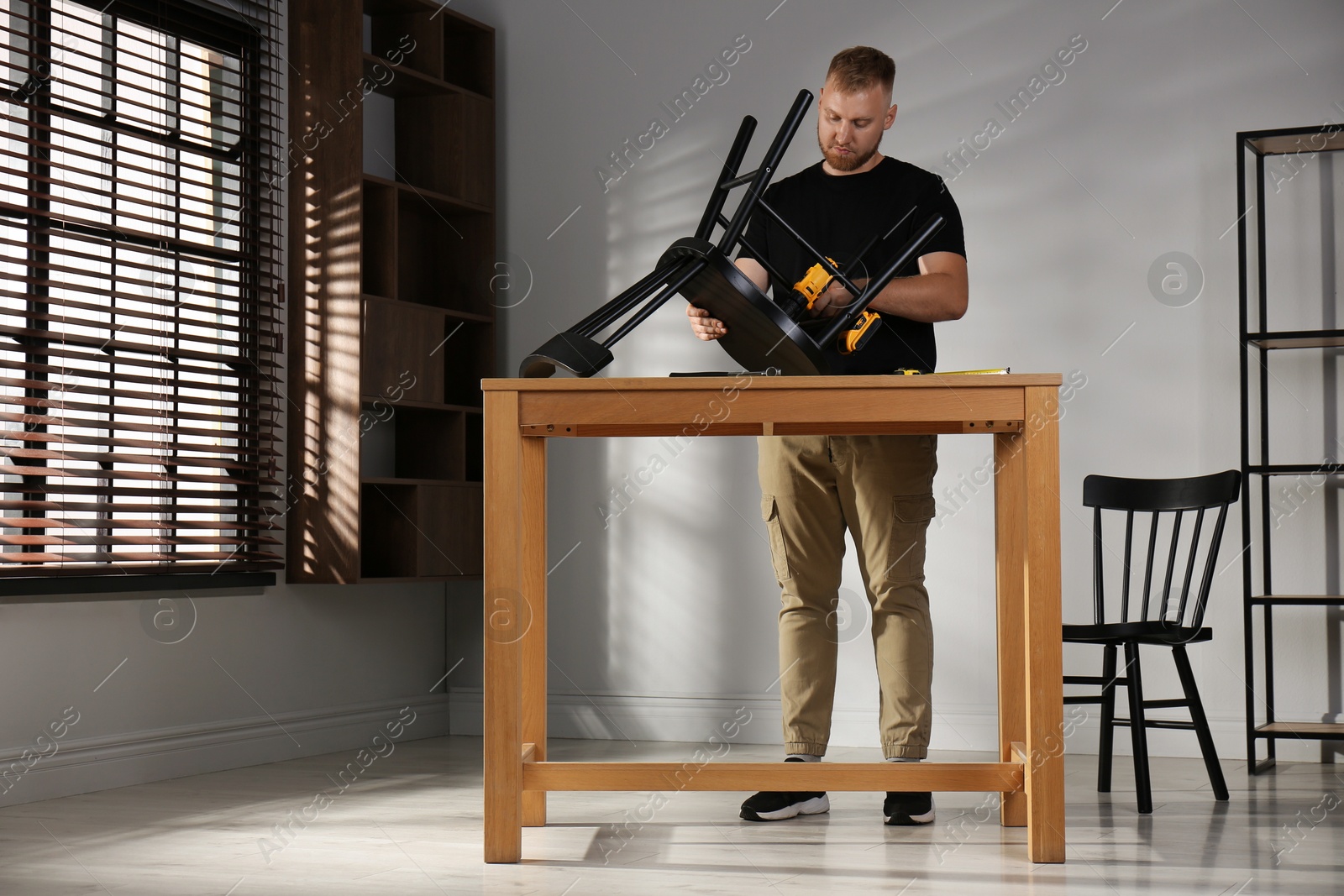 Photo of Man with electric screwdriver assembling chair in room