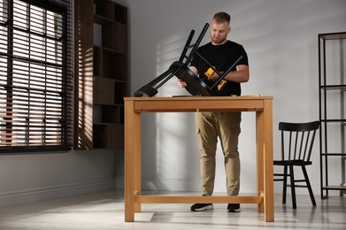 Photo of Man with electric screwdriver assembling chair in room