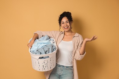 Happy woman with basket full of laundry on beige background