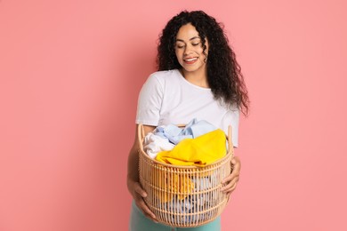 Photo of Happy woman with basket full of laundry on pink background