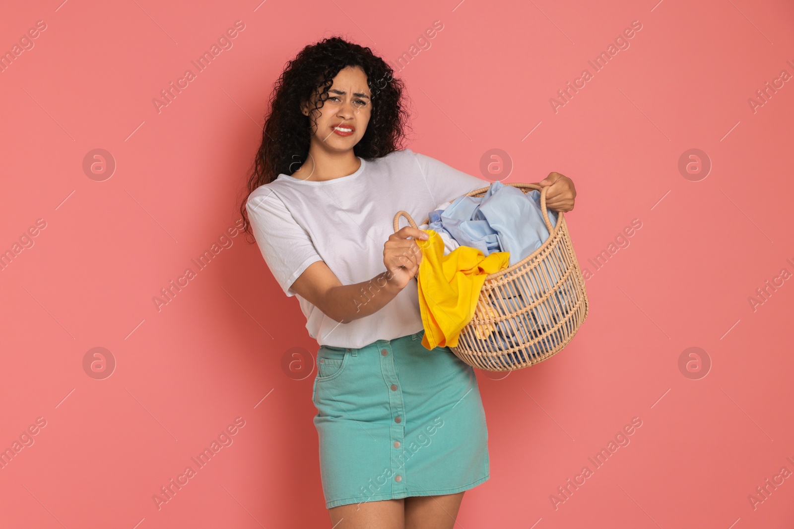 Photo of Displeased woman with basket full of laundry on pink background