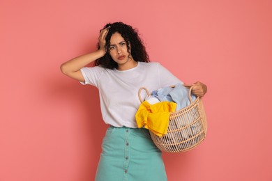 Displeased woman with basket full of laundry on pink background