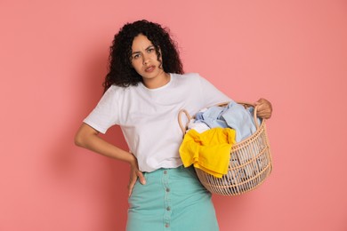 Photo of Displeased woman with basket full of laundry on pink background