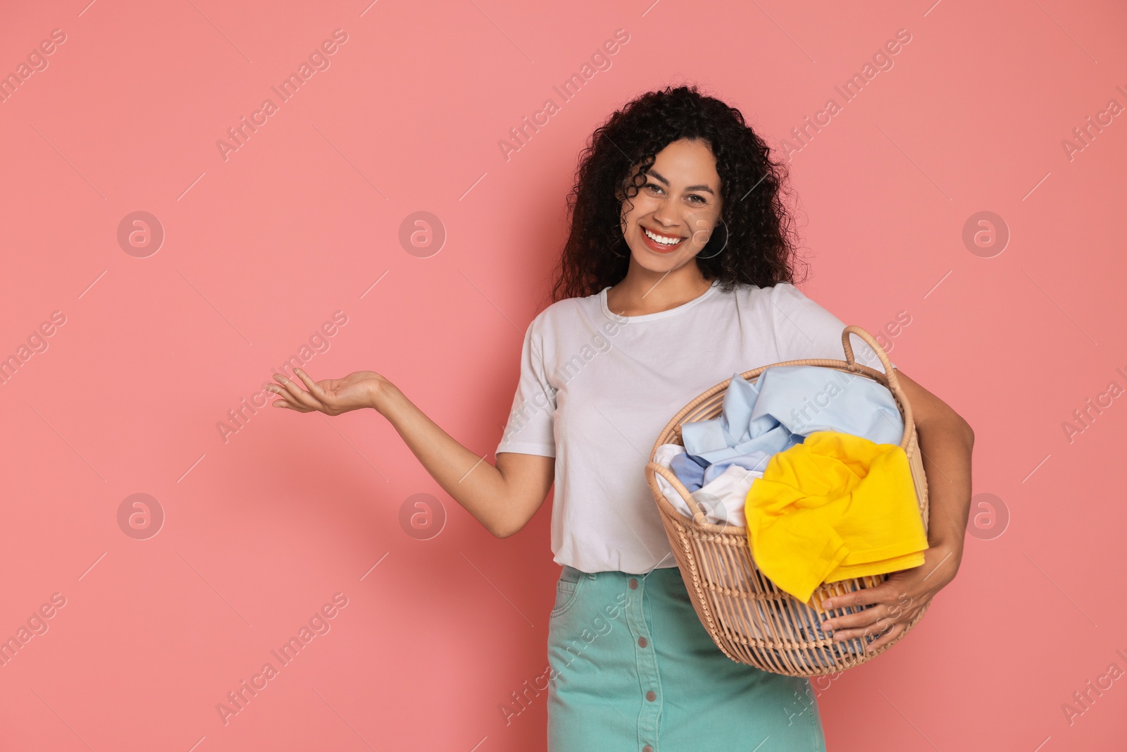 Photo of Happy woman with basket full of laundry on pink background