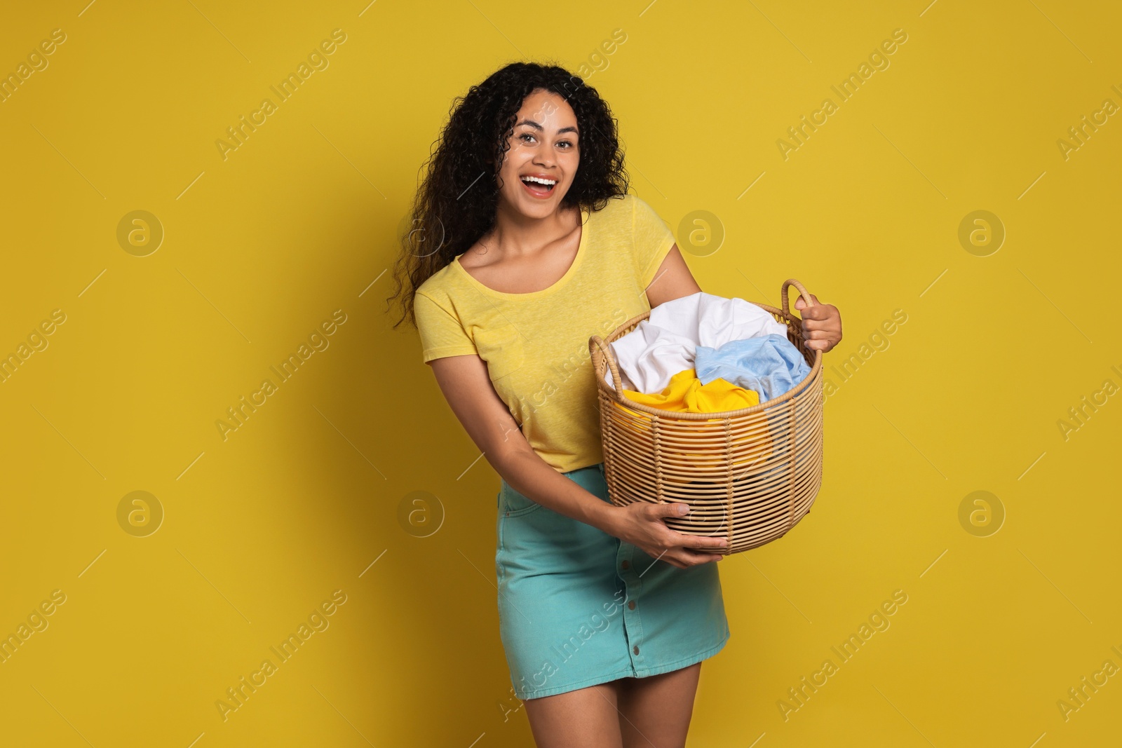 Photo of Happy woman with basket full of laundry on yellow background