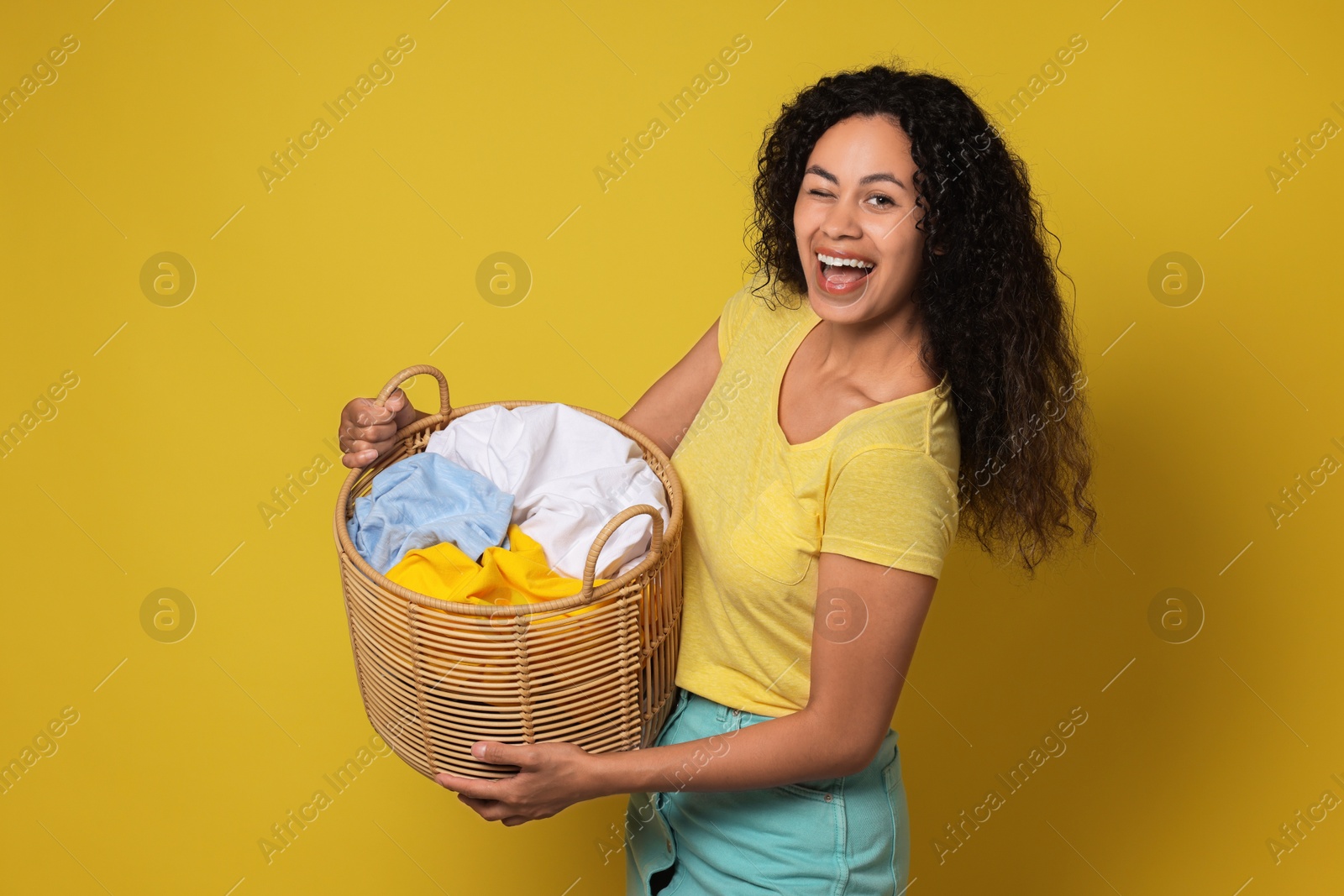 Photo of Happy woman with basket full of laundry on yellow background