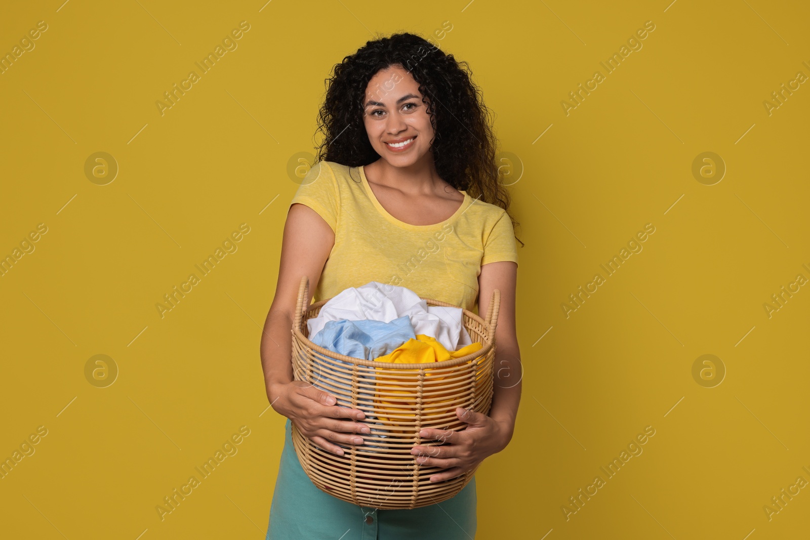 Photo of Happy woman with basket full of laundry on yellow background