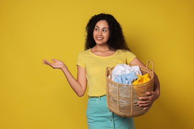 Photo of Happy woman with basket full of laundry on yellow background