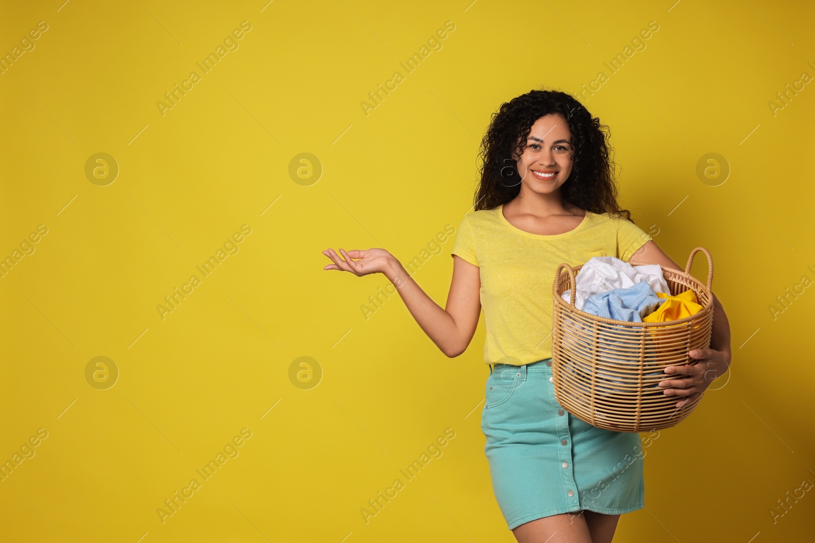 Photo of Happy woman with basket full of laundry on yellow background, space for text