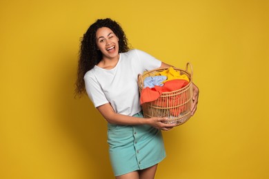 Photo of Happy woman with basket full of laundry on yellow background