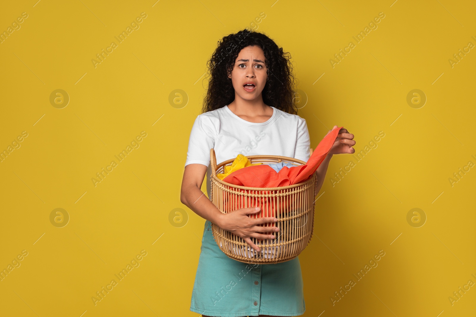 Photo of Displeased woman with basket full of laundry on yellow background