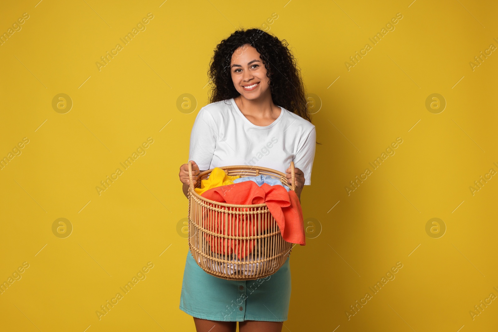 Photo of Happy woman with basket full of laundry on yellow background