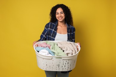 Photo of Happy woman with basket full of laundry on yellow background