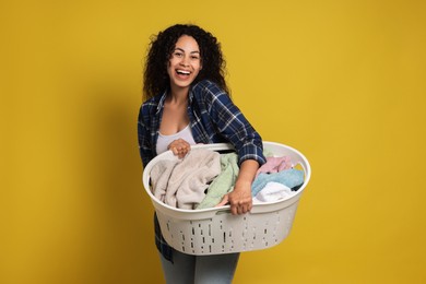 Happy woman with basket full of laundry on yellow background