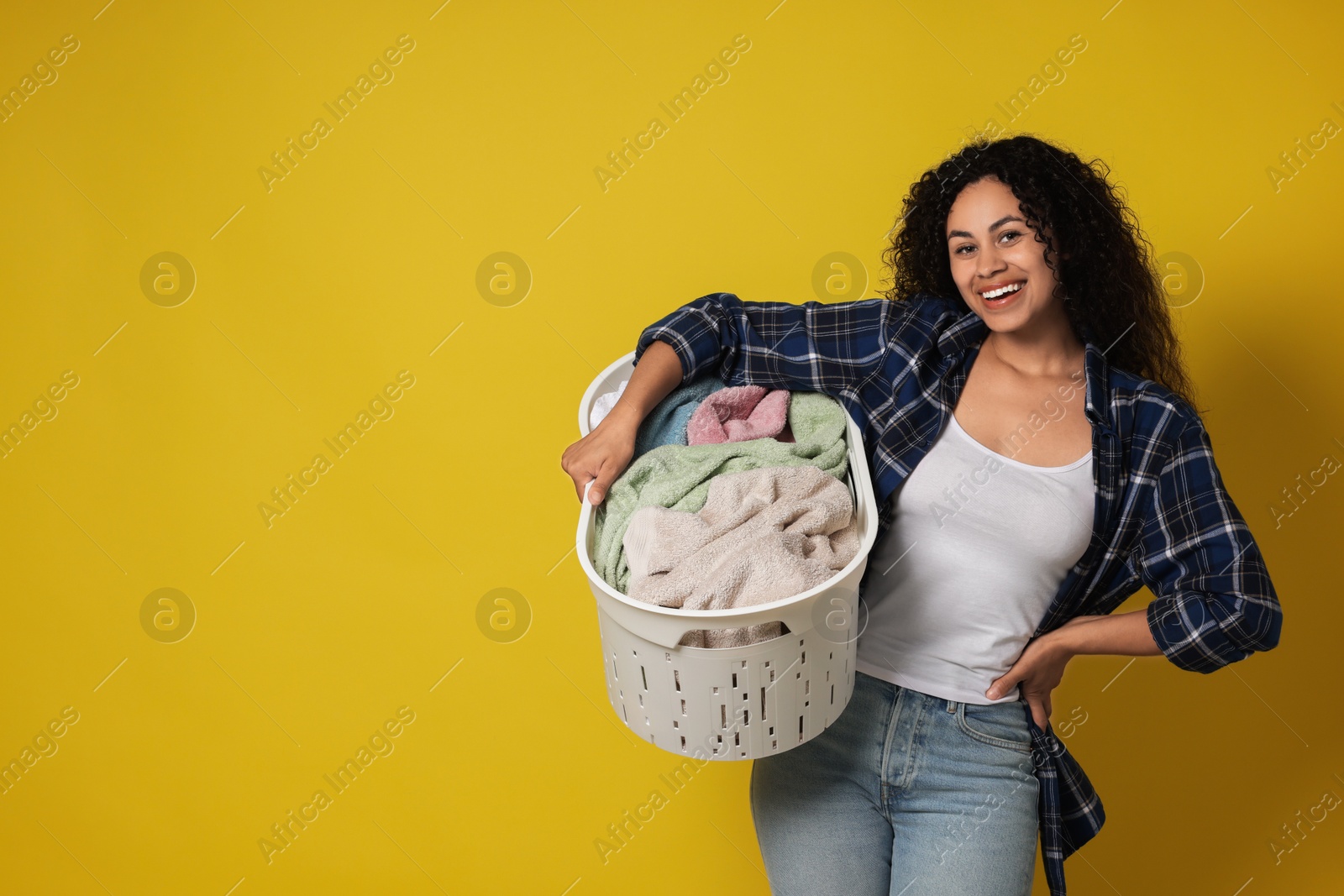 Photo of Happy woman with basket full of laundry on yellow background, space for text