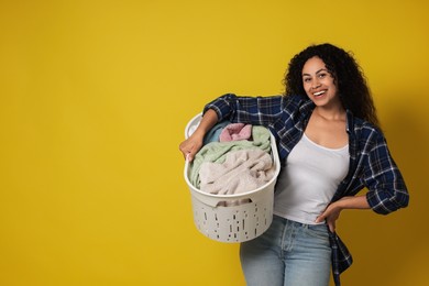 Happy woman with basket full of laundry on yellow background, space for text