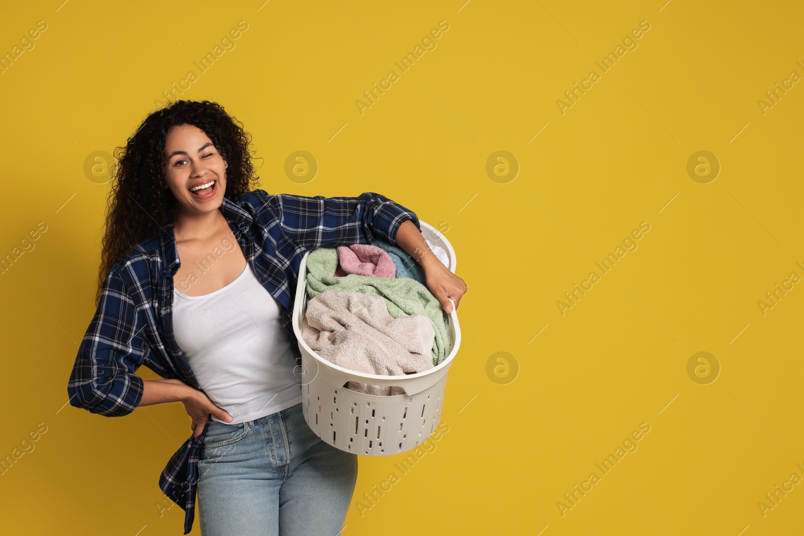 Photo of Happy woman with basket full of laundry on yellow background, space for text