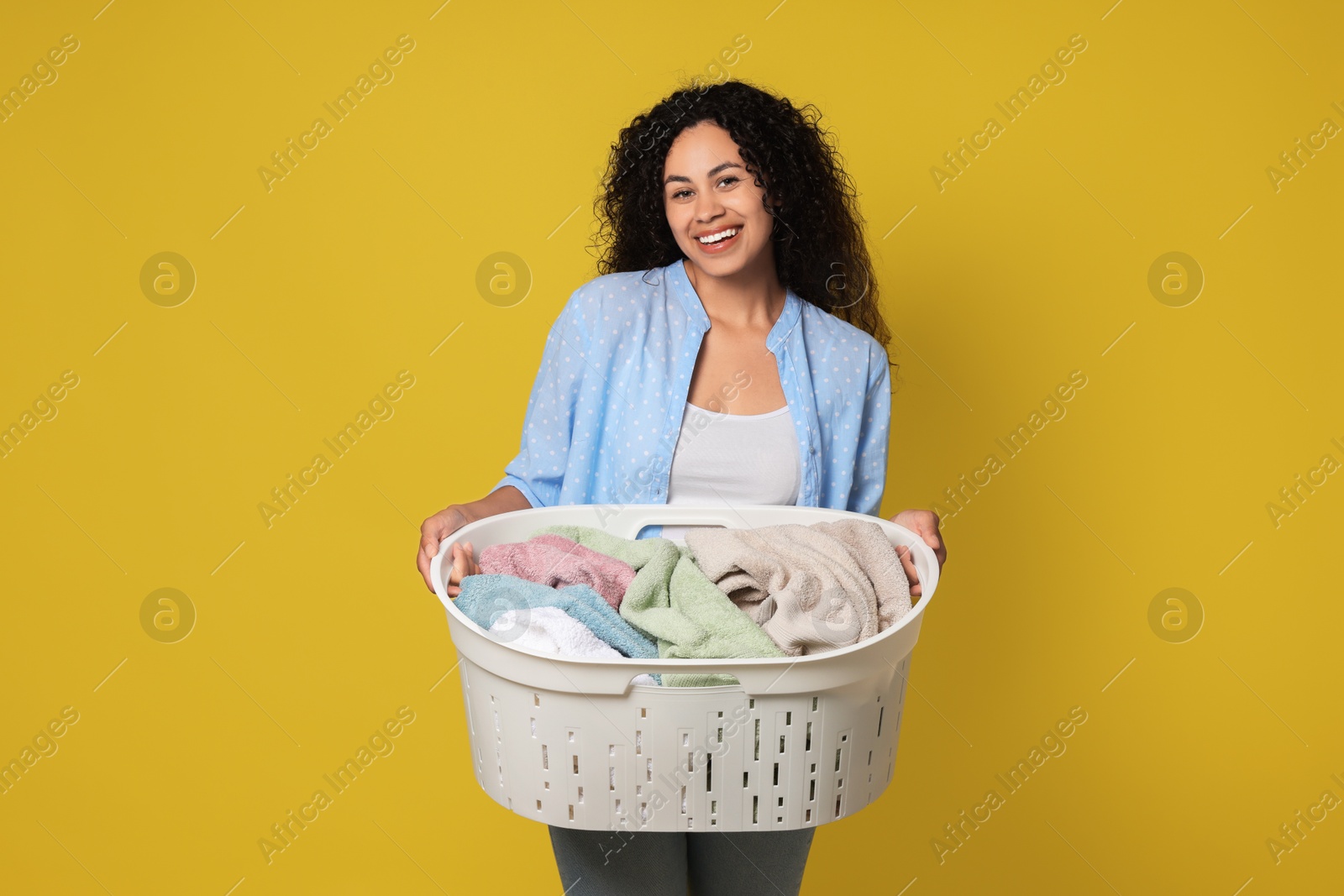 Photo of Happy woman with basket full of laundry on yellow background