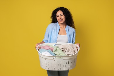 Happy woman with basket full of laundry on yellow background