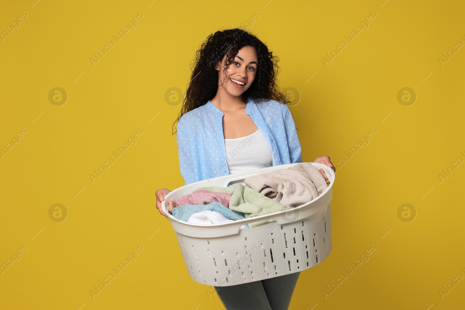 Photo of Happy woman with basket full of laundry on yellow background