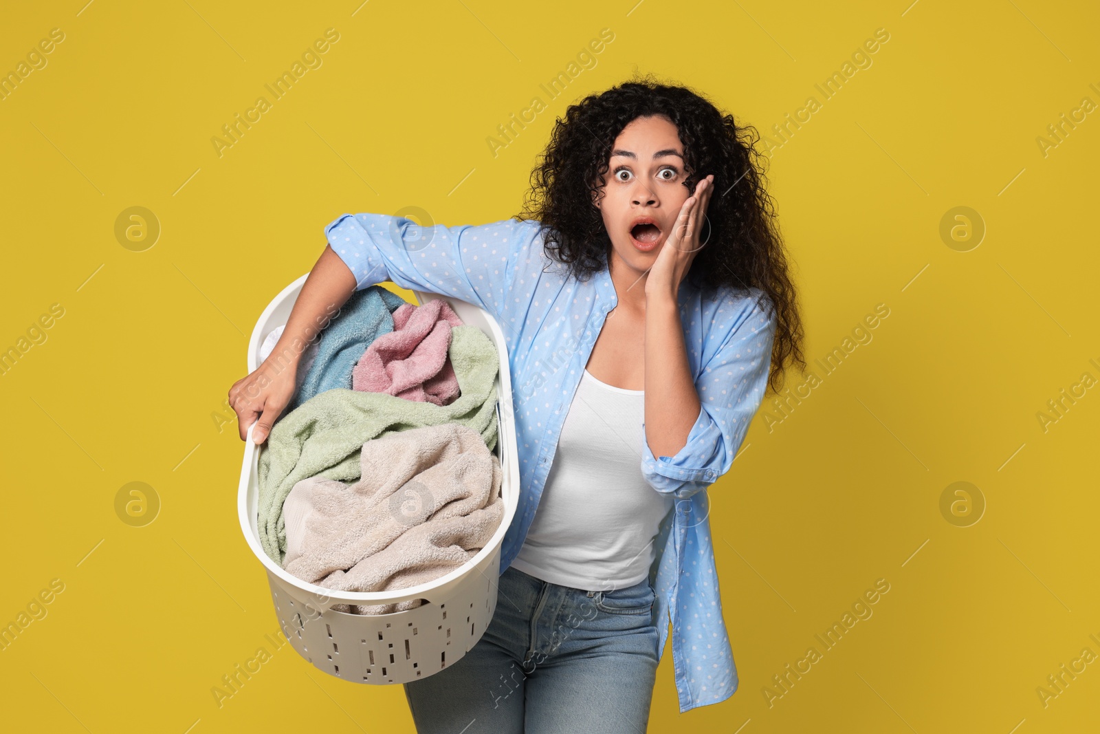 Photo of Shocked woman with basket full of laundry on yellow background