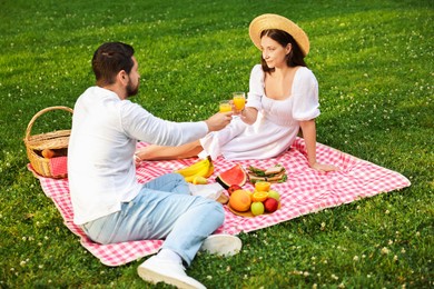 Lovely couple clinking glasses of juice on picnic blanket outdoors