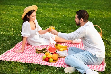 Photo of Lovely couple clinking glasses of juice on picnic blanket outdoors