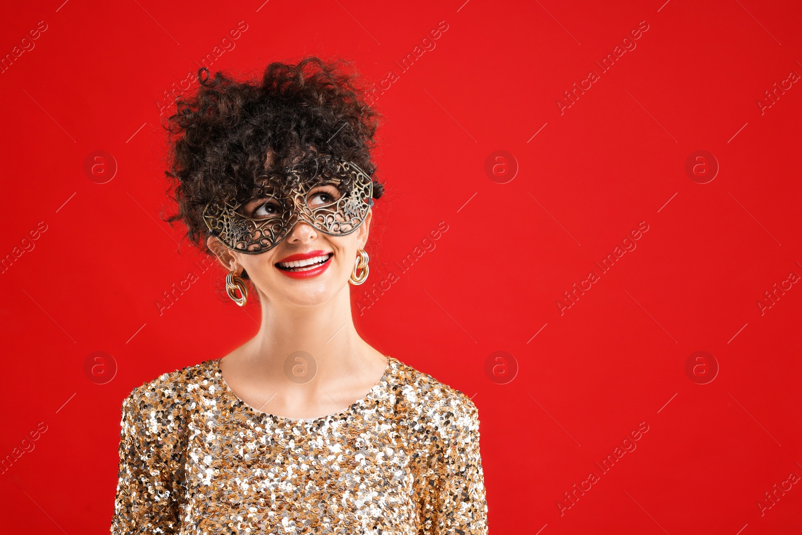 Photo of Smiling young woman wearing carnival mask on red background, space for text