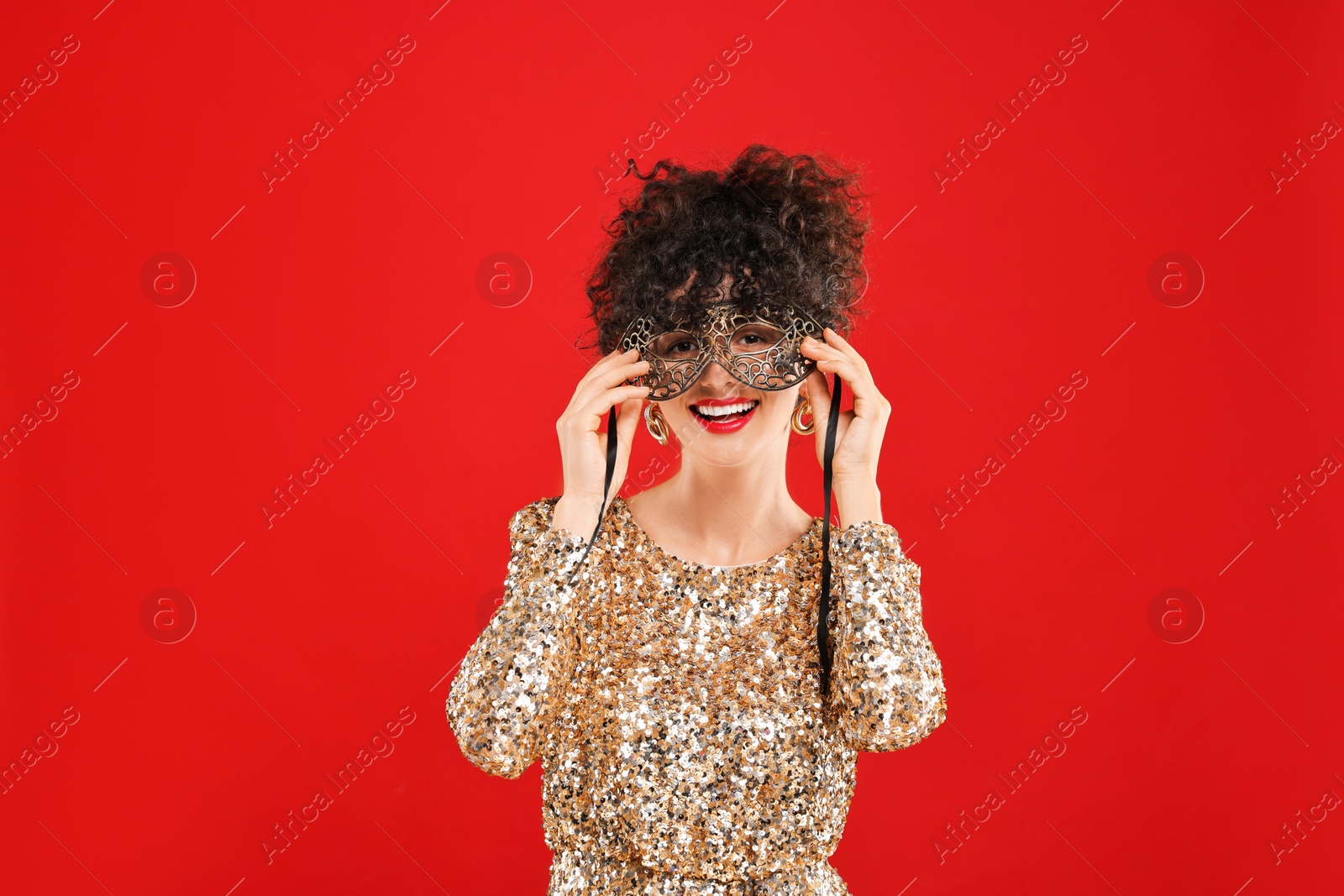 Photo of Smiling young woman wearing carnival mask on red background